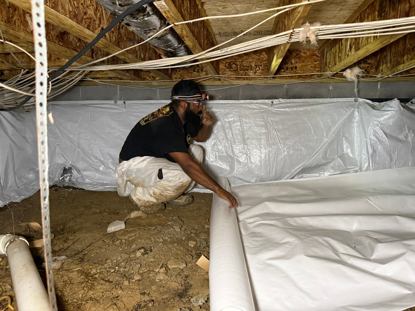 Crawl Space Ninja technician installing a 12 mil white crawl space vapor barrier during a professional crawl space encapsulation to reduce ground moisture and improve dehumidifier performance.
