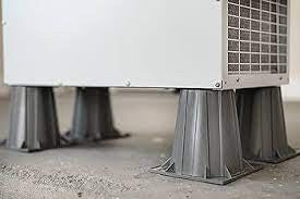 AprilAire dehumidifier elevated on risers in a crawl space, showing the clearance beneath the unit and support provided by the risers during installation.
